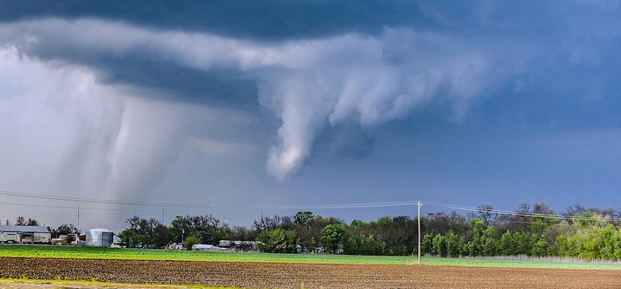 A funnel cloud turning into a tornado reaches down from the sky above a plowed field